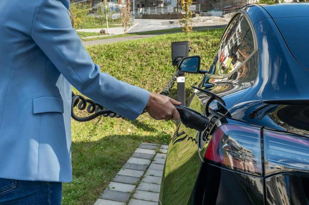 Person connecting an electric car to a charging station outdoors, showcasing green energy transition.
