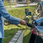 Person connecting an electric car to a charging station outdoors, showcasing green energy transition.